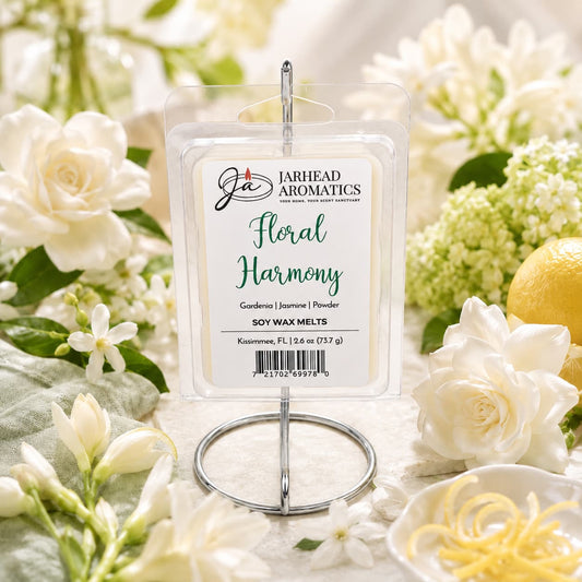 A package of Jarhead Aromatics Floral Harmony Soy Wax Melt | Gardenia, Jasmine & Tuberose is presented on a metal stand, surrounded by white flowers and lemon zest against a light, elegant background, emphasizing its floral fragrance and long-lasting scent.