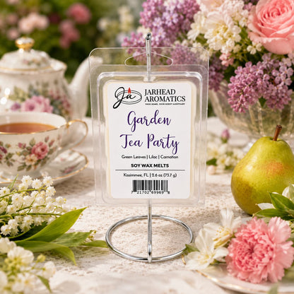 A package of Jarhead Aromatics Garden Tea Party Soy Wax Melt | Rose, Lilac & Jasmine is displayed on a table alongside a teacup, flowers, and a pear, evoking the inviting floral fragrance of a spring garden tea party setting.
