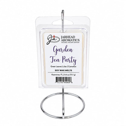 A package of Jarhead Aromatics Garden Tea Party Soy Wax Melt | Rose, Lilac & Jasmine sits elegantly on a silver metal stand. Infused with a charming floral fragrance, the label highlights notes of rose, lilac, and jasmine, perfectly capturing the essence of a tranquil garden tea party.