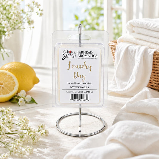 A package of Jarhead Aromatics Laundry Day Soy Wax Melt | Fresh Linen, Lemon & Clean Musk is displayed on a metal stand, surrounded by fresh lemons, white towels, and sunlight in the background. The scene evokes a crisp and clean atmosphere, perfectly capturing the essence of this home fragrance that infuses any space with notes of fresh linen, zesty lemon, and clean musk.
