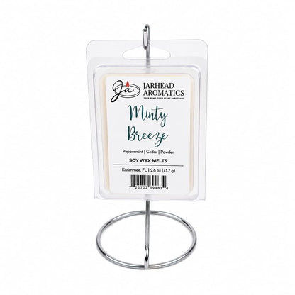 A package of Jarhead Aromatics Minty Breeze Soy Wax Melt | Peppermint, Eucalyptus & Cedarwood is displayed on a metal stand. The label highlights peppermint, eucalyptus, and cedarwood scents, as well as the wax weight and origin. Infused with a refreshing peppermint eucalyptus fragrance, this soy wax melt from Jarhead Aromatics creates a relaxing atmosphere that’s perfect for any space.