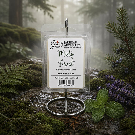 A package of Jarhead Aromatics Misty Forest Soy Wax Melt | Moss, Juniper & Rain-Kissed Woods is showcased on a metal stand in a misty forest, surrounded by green moss, ferns, and purple flowers, capturing the essence of natural home fragrance with its enchanting blend of moss, juniper, and rain-kissed woods.