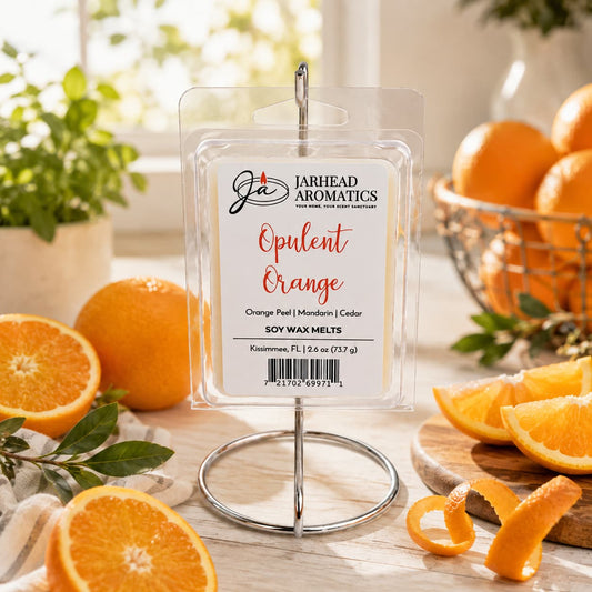 A package of Jarhead Aromatics Opulent Orange Soy Wax Melt | Orange, Grapefruit & Lemon is displayed on a stand, surrounded by fresh oranges, orange slices, and greenery on a sunlit table—perfect for filling your space with the vibrant citrus home fragrance of orange, grapefruit, and lemon.