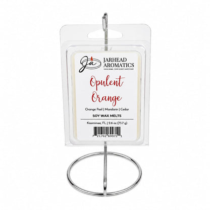 A clear, rectangular package of Jarhead Aromatics’ Opulent Orange Soy Wax Melt—infused with orange, grapefruit, and lemon—is showcased on a silver metal stand. The label highlights bright citrus fragrance notes and features the premium soy wax formula.