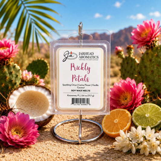 A package of Jarhead Aromatics’ Prickly Petals Soy Wax Melt | Cactus Flower, Coconut & Sandalwood is displayed outdoors among cacti, pink cactus blooms, sliced citrus, and desert mountains beneath a sunny sky. The vibrant and natural scene captures the inviting essence of home fragrance inspired by the beauty of the desert.