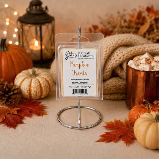 A pack of Jarhead Aromatics Pumpkin Treats Soy Wax Melt | Pumpkin, Caramel & Maple Pecan sits on a stand—hand-poured soy wax infused with the delectable aroma of pumpkin, caramel, and maple pecan—surrounded by pumpkins, autumn leaves, a lantern, a cozy blanket, and a mug of hot chocolate topped with whipped cream.