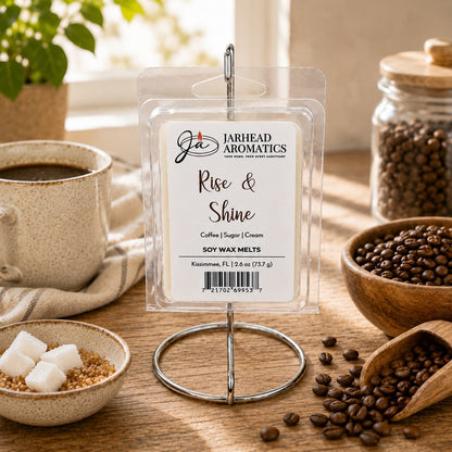 A package of Jarhead Aromatics Rise & Shine Soy Wax Melt | Fresh Coffee, Sugar & Cream rests on a metal holder, surrounded by a coffee cup, a bowl of coffee beans, sugar cubes, and a jar of beans on a sunlit table, filling the air with the inviting aroma of fresh coffee blended with sugar and cream.