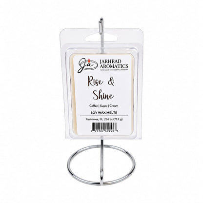A hand-poured package of Jarhead Aromatics Rise & Shine Soy Wax Melt | Fresh Coffee, Sugar & Cream rests on a metal stand. The label showcases its inviting blend of fresh coffee, sugar, and cream fragrances. Each package contains 2.6 oz (73 g) of aromatic delight.