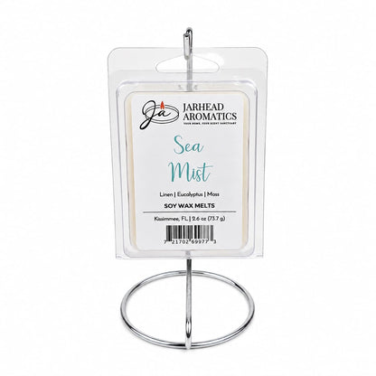 A package of Jarhead Aromatics Sea Mist Soy Wax Melt | Fresh Linen, Sea Salt & Eucalyptus is displayed upright on a silver metal stand. The label highlights notes of fresh linen, sea salt, and eucalyptus, evoking a spa-inspired aroma and bringing a refreshing coastal fragrance to your space.