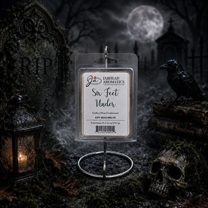 A package of Jarhead Aromatics’ Six Feet Under Soy Wax Melt | Damp Earth, Moss & Ancient Oak stands on a holder in a spooky graveyard, surrounded by a skull, raven, lantern, and tombstones beneath a full moon, with a Book of Shadows nearby. The scene mirrors the dark and atmospheric fragrance infused in every melt.
