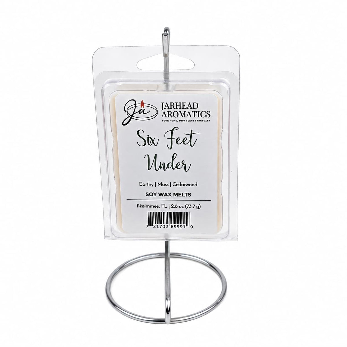 A package of Jarhead Aromatics’ Six Feet Under Soy Wax Melt | Damp Earth, Moss & Ancient Oak is displayed on a silver stand. The clear, rectangular packaging features a label that highlights its damp earth, moss, and ancient oak scents. This dark and atmospheric fragrance truly captures the essence of Six Feet Under, filling any space with a mysterious and captivating aroma.