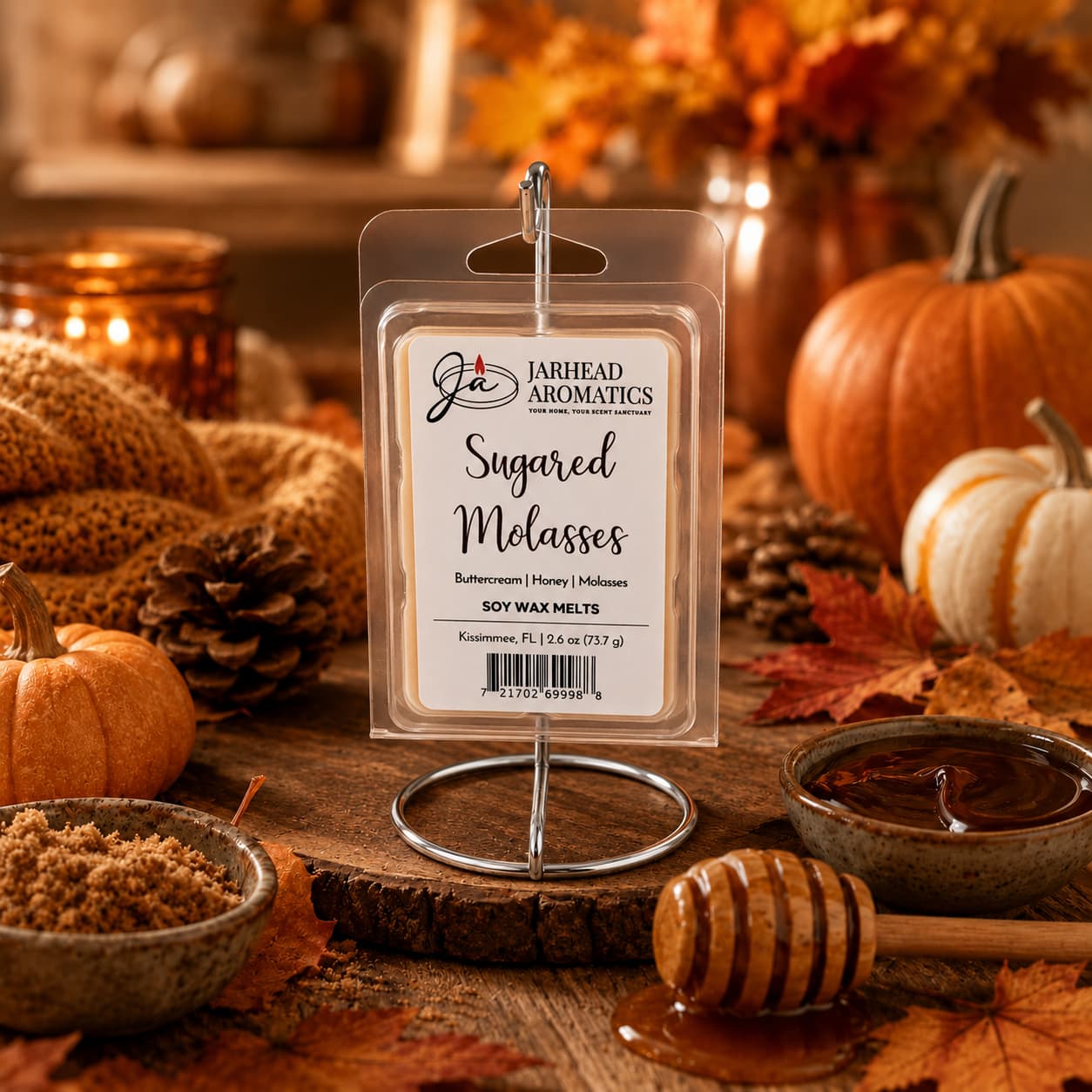 A pack of Sugared Molasses Soy Wax Melt | Buttercream, Honey & Dark Molasses by Jarhead Aromatics is displayed on a stand, surrounded by pumpkins, autumn leaves, brown sugar, and honey for a warm and cozy fall ambiance. This highly fragrant wax melt is hand-poured with premium soy wax to deliver a long-lasting autumn scent experience.