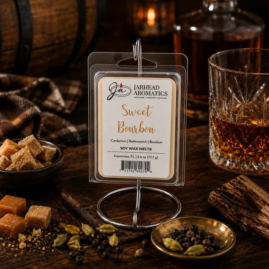 A package of Jarhead Aromatics’ Sweet Bourbon Soy Wax Melt | Bourbon, Butterscotch & Brown Sugar—a gourmand blend celebrated for its long-lasting scent—is showcased on a metal stand, surrounded by a glass of bourbon, brown sugar cubes, cardamom pods, peppercorns, and butterscotch atop a rustic wooden table.