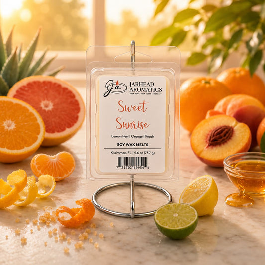 A package of Jarhead Aromatics’ Sweet Sunrise Soy Wax Melt | Lemon, Orange & Juicy Peach is displayed on a stand, surrounded by fresh citrus fruits, a peach, honey in a dish, and curly citrus peels, with sunlight streaming through the window in the background. This inviting scene captures the vibrant essence of this citrus home fragrance, perfect for brightening any space.