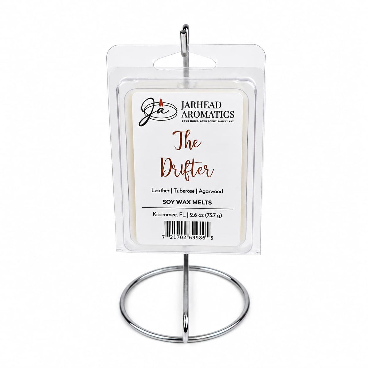 A package of Jarhead Aromatics The Drifter Soy Wax Melt | Leather, Agarwood & Tuberose sits on a silver metal stand. The label highlights its blend of leather, agarwood, and tuberose notes for an Old West-inspired fragrance. The background is plain white.