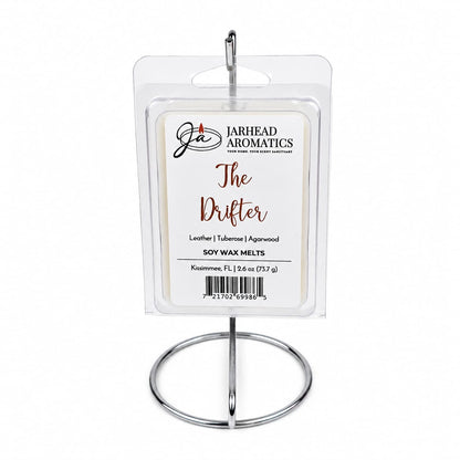 A package of Jarhead Aromatics The Drifter Soy Wax Melt | Leather, Agarwood & Tuberose sits on a silver metal stand. The label highlights its blend of leather, agarwood, and tuberose notes for an Old West-inspired fragrance. The background is plain white.