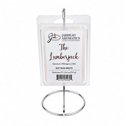 A clamshell package labeled The Lumberjack Soy Wax Melt by Jarhead Aromatics is displayed on a metal stand. Infused with a rich woodsy fragrance, the scent notes listed are mahogany, cedarwood, and oak.