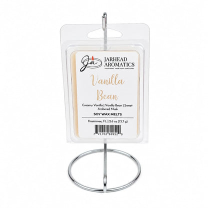A package of Jarhead Aromatics Vanilla Bean Soy Wax Melt | Creamy Vanilla & Amber Musk sits elegantly on a silver display stand, with text describing its irresistible home fragrance and product details. These premium soy wax melts fill your space with a warm blend of creamy vanilla and amber musk, creating an inviting atmosphere in any room.