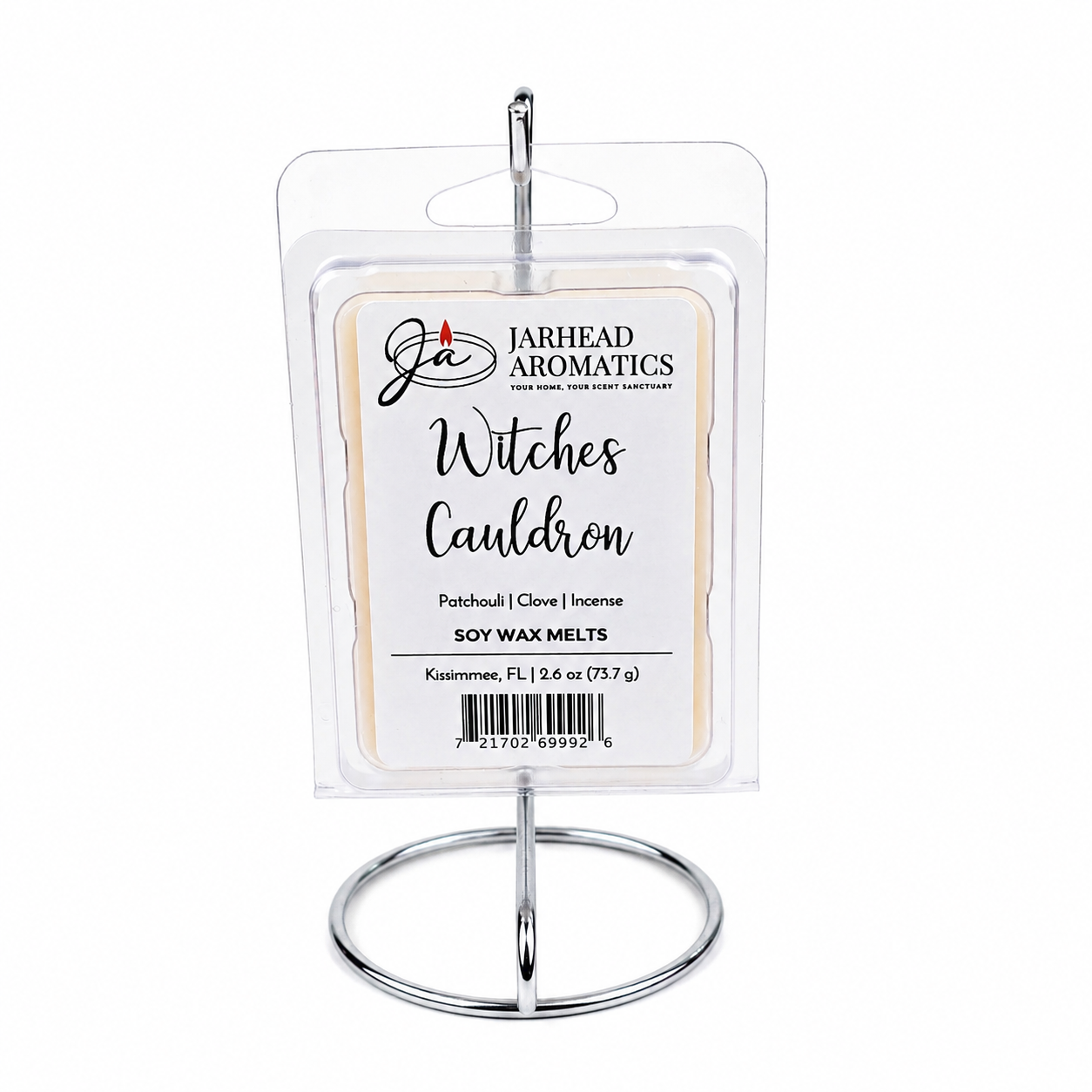 A package of Jarhead Aromatics Witches Cauldron Soy Wax Melt | Orange Blossom, Patchouli & Dark Incense sits atop a silver display stand. The label showcases notes of orange blossom, patchouli, and dark incense for a highly fragrant experience, and features a barcode at the bottom.