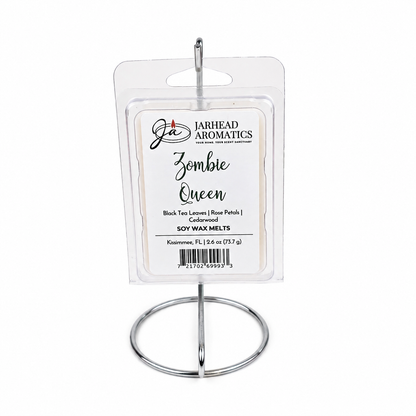 A package of Jarhead Aromatics Zombie Queen Soy Wax Melt | Black Tea, Rose Petals & Cedarwood is displayed upright on a silver metal stand against a white background, highlighting its distinctive blend of floral and smoky black tea fragrance.