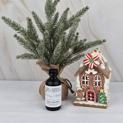 A small frosted pine tree, a gingerbread house decor, and Jarhead Aromatics' Merry & Bright Room/Linen Spray from the Winter Collection create a cozy scene, perfect for bringing festive fragrance to your space.
