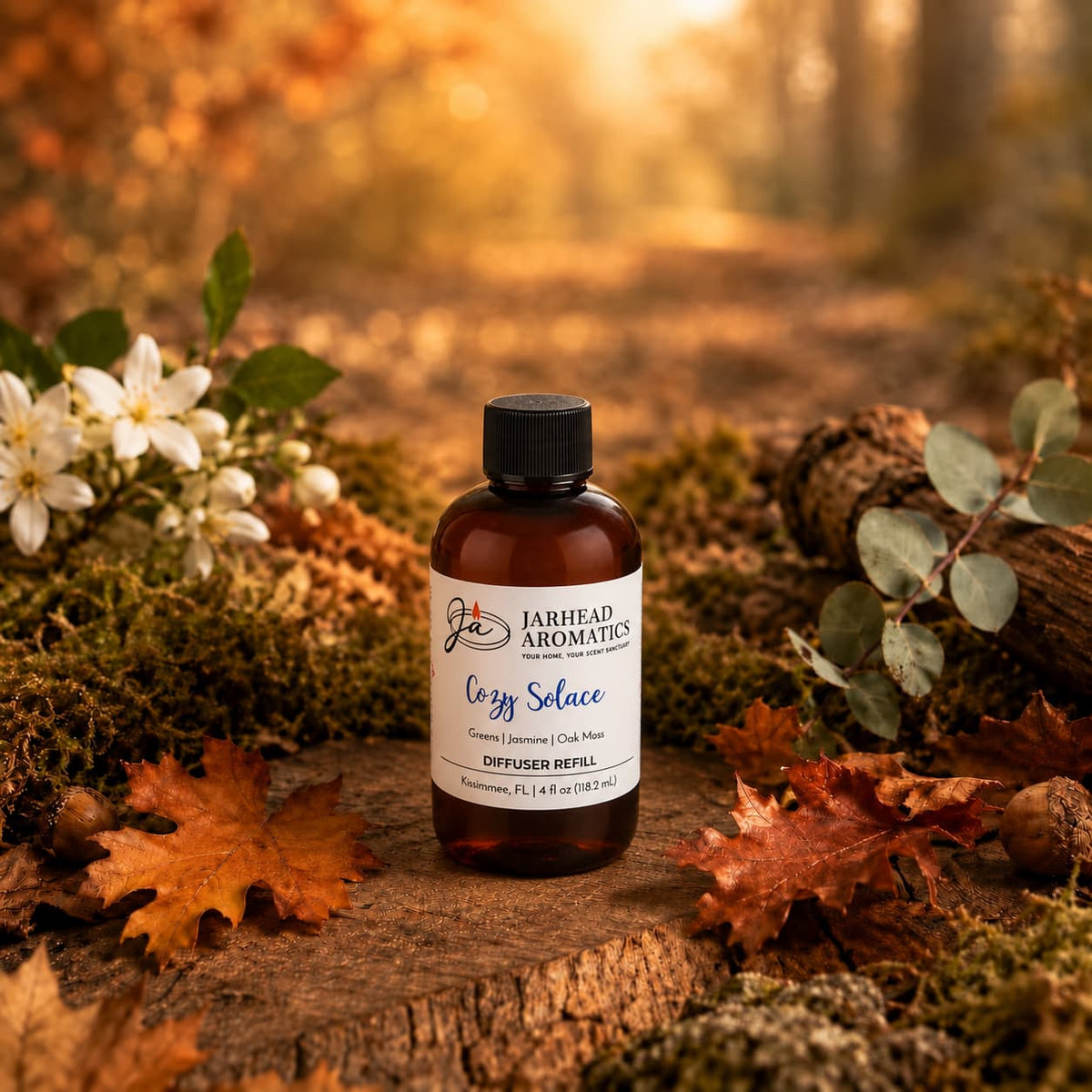 A bottle of Jarhead Aromatics Cozy Solace Diffuser Refill, featuring notes of fresh greens, jasmine, and oak moss, rests on a bed of moss surrounded by fallen autumn leaves and delicate flowers in a sun-dappled forest scene.