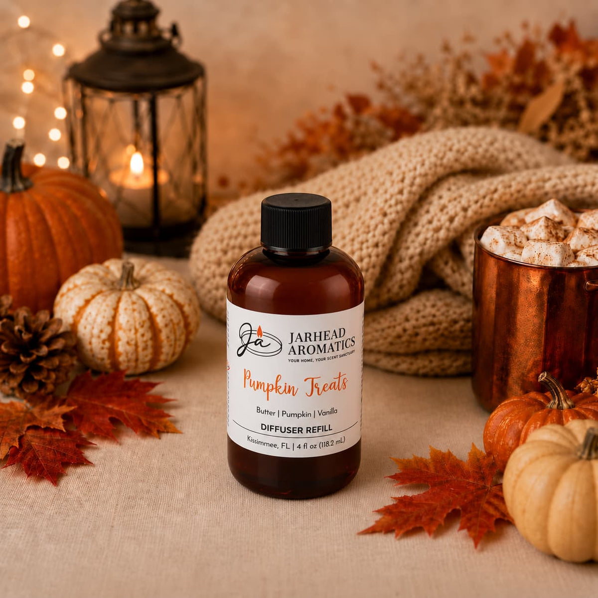 A bottle of Jarhead Aromatics’ Pumpkin Treats Diffuser Refill | Pumpkin, Caramel & Maple Pecan sits on a table surrounded by pumpkins, autumn leaves, a knit blanket, a lantern, and a mug of marshmallows—creating a cozy fall atmosphere enriched by its inviting pumpkin spice fragrance.
