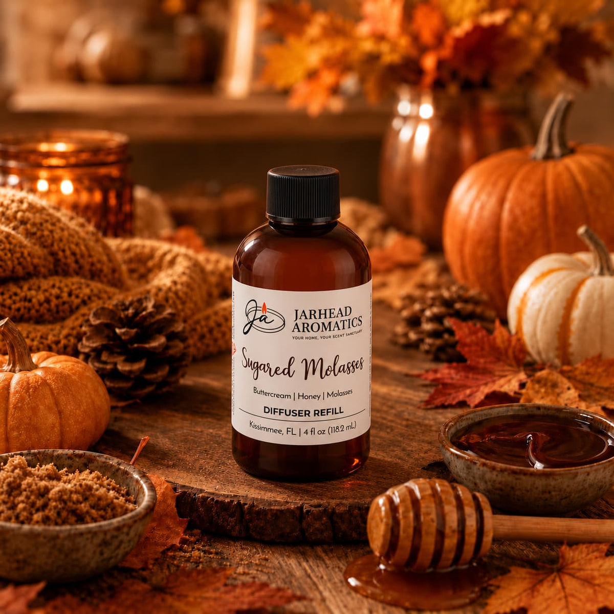 A bottle of Jarhead Aromatics Sugared Molasses Diffuser Refill | Buttercream, Honey & Dark Molasses rests on a rustic table adorned with autumn decor—pumpkins, brown sugar, a honey dipper, and candles—creating a cozy atmosphere and filling your home with an inviting blend of buttercream, honey, and dark molasses for the ultimate autumn fragrance experience.