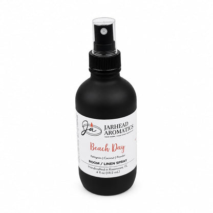 A black spray bottle labeled Jarhead Aromatics Beach Day Room & Linen Spray offers a beach-inspired home fragrance with notes of citrus, coconut, and coastal musk. Handcrafted in Kissimmee, FL, this tropical room and linen spray contains 4 fl oz to freshen any space.