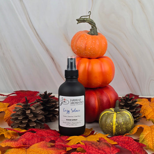 Jarhead Aromatics Cozy Solace – Room Spray (Fall Collection) is displayed among pumpkins, pinecones, and autumn leaves, creating a festive fall scene with notes of oak moss and fresh greens.