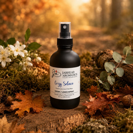 A dark bottle of Jarhead Aromatics’ Cozy Solace Room & Linen Spray, with fresh greens, jasmine, and oak moss notes, rests on a mossy forest floor surrounded by autumn leaves and acorns, bathed in gentle sunlight—inviting a distinct home fragrance experience.