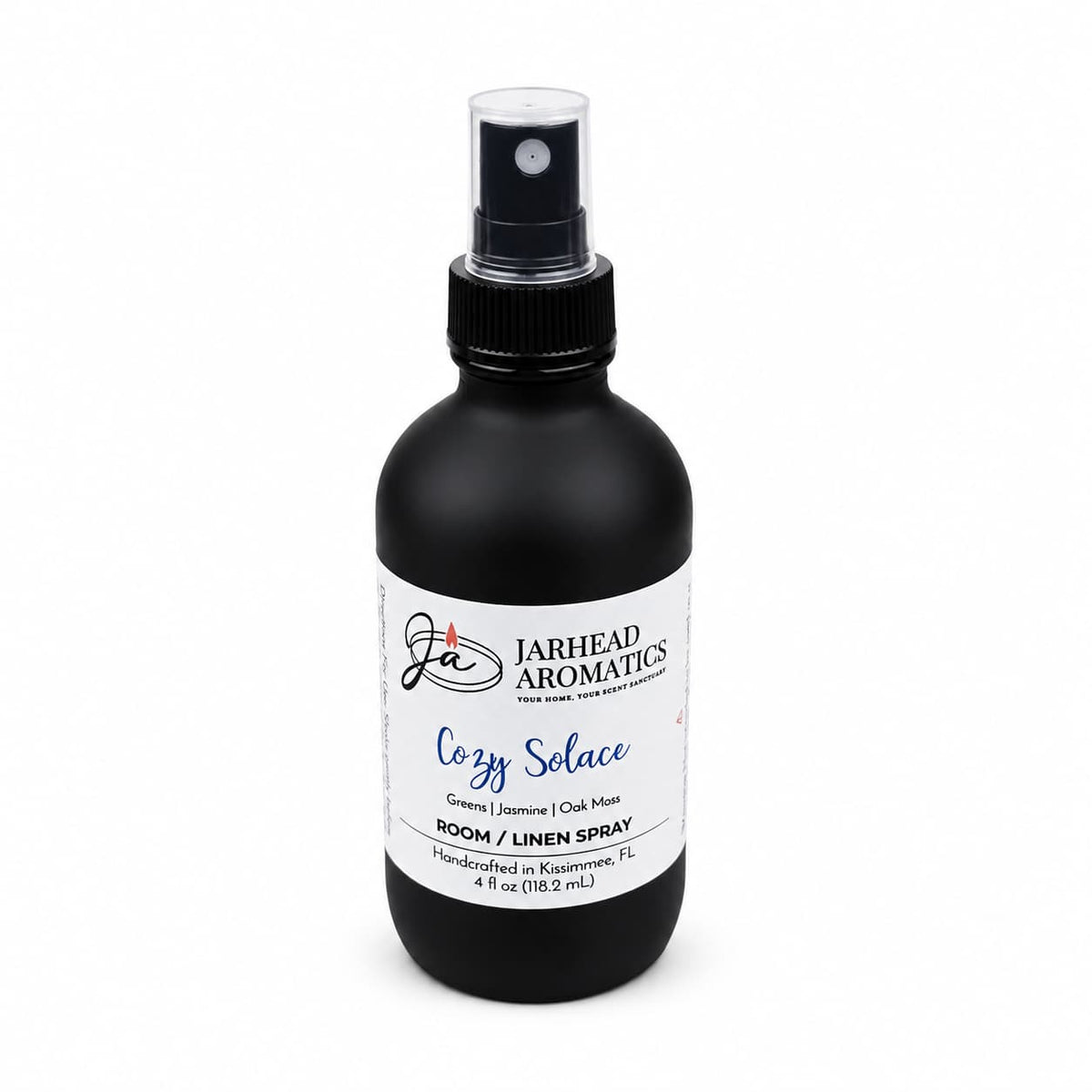 A black spray bottle labeled with a white and blue design displays the Jarhead Aromatics brand, featuring their Cozy Solace Room & Linen Spray. Handcrafted in Florida, this unique home fragrance blends fresh greens, jasmine, and oak moss.