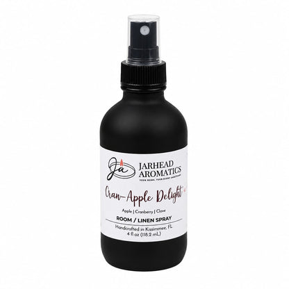 A black spray bottle labeled Jarhead Aromatics Cran-Apple Delight Room & Linen Spray offers a cozy blend of cranberry, apple, and warm cinnamon for an inviting home fragrance. This handcrafted 4 fl oz bottle is made in Kissimmee, FL.