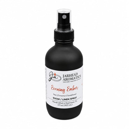 A black spray bottle labeled Jarhead Aromatics Evening Ember Room & Linen Spray, 4 fl oz, fills any space with a warm home fragrance featuring notes of plum, sandalwood, and soft smoke. The white-labeled bottle with a black cap is perfect for refreshing your room or linens.