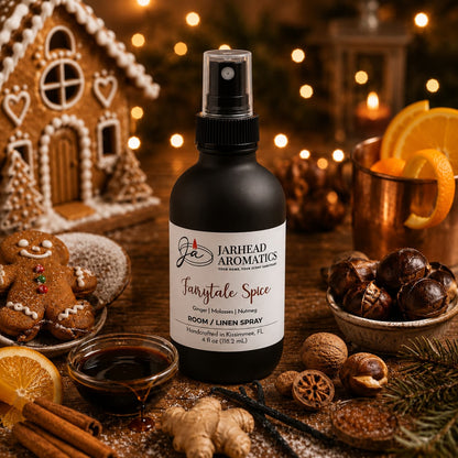 A bottle of Jarhead Aromatics Fairytale Spice Room & Linen Spray | Gingerbread, Molasses & Warm Spice is nestled among festive holiday accents—gingerbread cookies, orange slices, spices, copper mugs, and twinkling Christmas lights—evoking the warmth and coziness of a bakery-inspired home fragrance with comforting notes reminiscent of a gingerbread house.