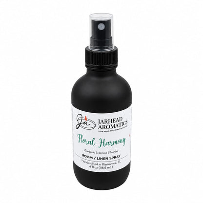 A black 4 oz spray bottle labeled Jarhead Aromatics contains the Floral Harmony Room & Linen Spray, a home fragrance that blends gardenia, jasmine, and tuberose for a refreshing floral scent.