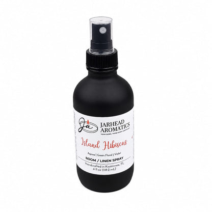 A black spray bottle labeled Jarhead Aromatics Island Hibiscus Room & Linen Spray features a fresh, tropical fragrance with notes of honeydew, lime, and tropical florals. This 4 oz linen spray is handcrafted in Kissimmee, FL, perfect for adding an island-inspired touch to any space.