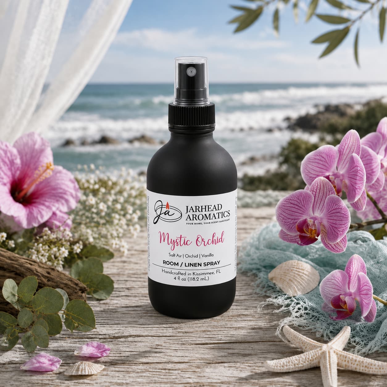 A bottle of Jarhead Aromatics Mystic Orchid Room & Linen Spray | Orchid, Salt Air & Vanilla rests on a wooden surface surrounded by pink orchids, a starfish, and seashells, filling the air with notes of coastal florals and vanilla. The ocean and blooms in the background highlight the fresh elegance of this exquisite home fragrance.