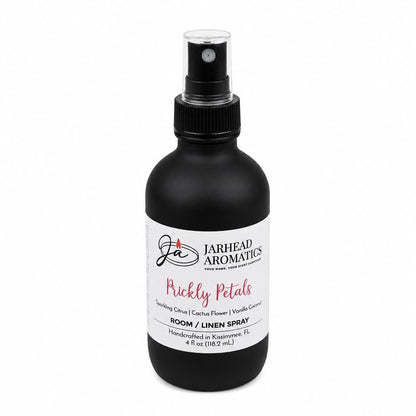 A black spray bottle labeled Jarhead Aromatics Prickly Petals Room & Linen Spray features a desert oasis blend of cactus flower, coconut, and sandalwood. The 4 oz bottle is handcrafted in Kissimmee, FL.
