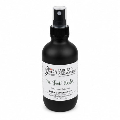 A handcrafted 4 oz black spray bottle labeled Jarhead Aromatics Six Feet Under Room & Linen Spray | Damp Earth, Moss & Ancient Oak offers an earthy home fragrance with notes of moss and ancient oak. Made in Kissimmee, FL, it’s a perfect addition to your home fragrance collection.