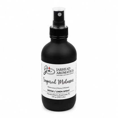 A black spray bottle of Jarhead Aromatics Sugared Molasses Room & Linen Spray, featuring notes of buttercream, honey, and dark molasses. This gourmand home fragrance doubles as both a linen spray and room refresher, comes in a 4 fl oz (118.2 mL) size, and is handcrafted in Kissimmee, FL.