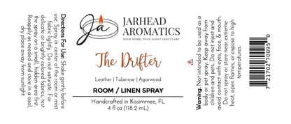 White label for Jarhead Aromatics The Drifter Room & Linen Spray | Leather, Tuberose & Smoky Agarwood, featuring usage directions, scent notes describing a western-inspired blend of leather, tuberose, and smoky agarwood, warning information, barcode, and a candle flame logo positioned above the brand name. Perfect as a leather home fragrance.