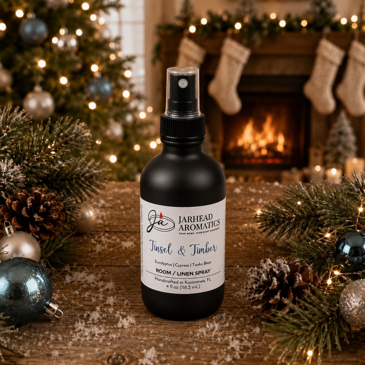 A black bottle of Jarhead Aromatics Tinsel & Timber Room & Linen Spray sits on a wooden table surrounded by Christmas decorations, with a fireplace in the background.