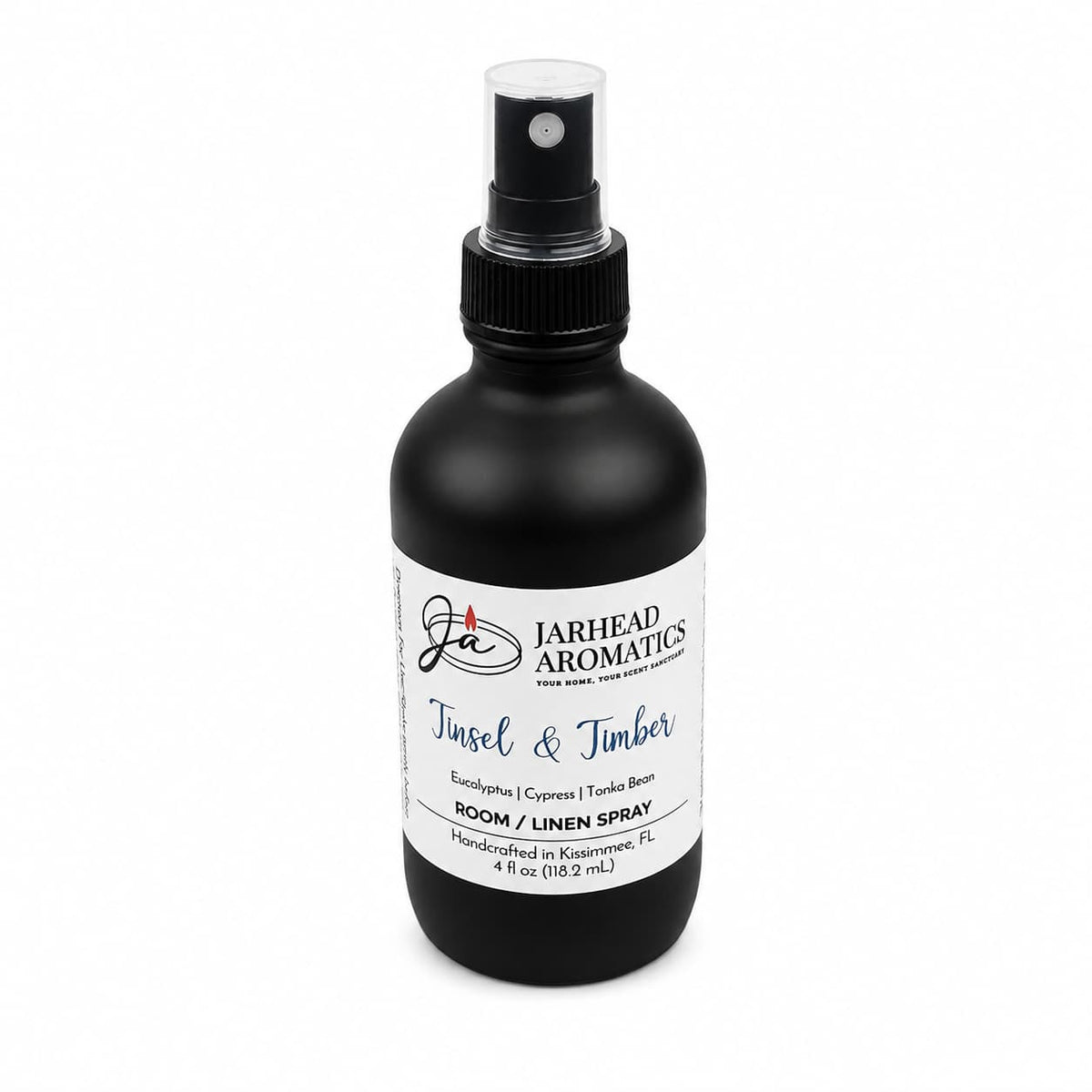 A black spray bottle with a white label reading Tinsel & Timber Room & Linen Spray, listing notes of eucalyptus, pine, smoke, and tonka bean for a winter forest scent.