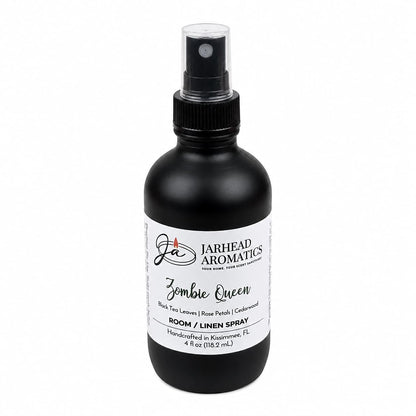A 4 oz black bottle of Jarhead Aromatics Zombie Queen Room & Linen Spray features a spray nozzle and a white label highlighting its scent notes of black tea, rose petals, and cedarwood. This dark floral room and linen spray is ideal for those who desire a gothic-inspired home fragrance.