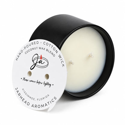 A two-wick black Coconut Wax Blend Candle, topped with a circular paper label reading hand-poured coconut wax blend and safety instructions to remove before lighting.