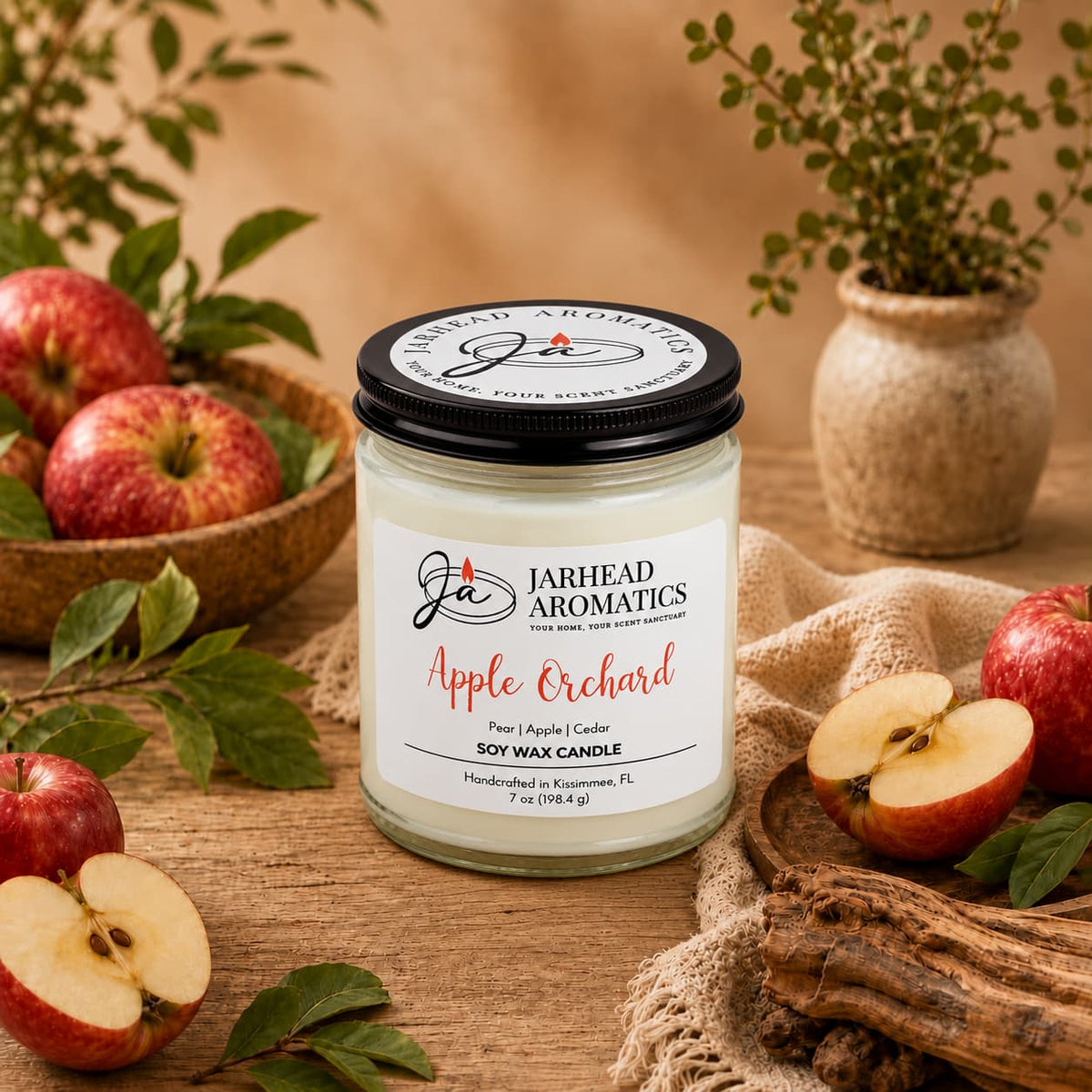 A Jarhead Aromatics Apple Orchard Soy Wax Candle | Pear, Apple & Cedar sits on a wooden table surrounded by fresh apples, apple slices, and small green plants.