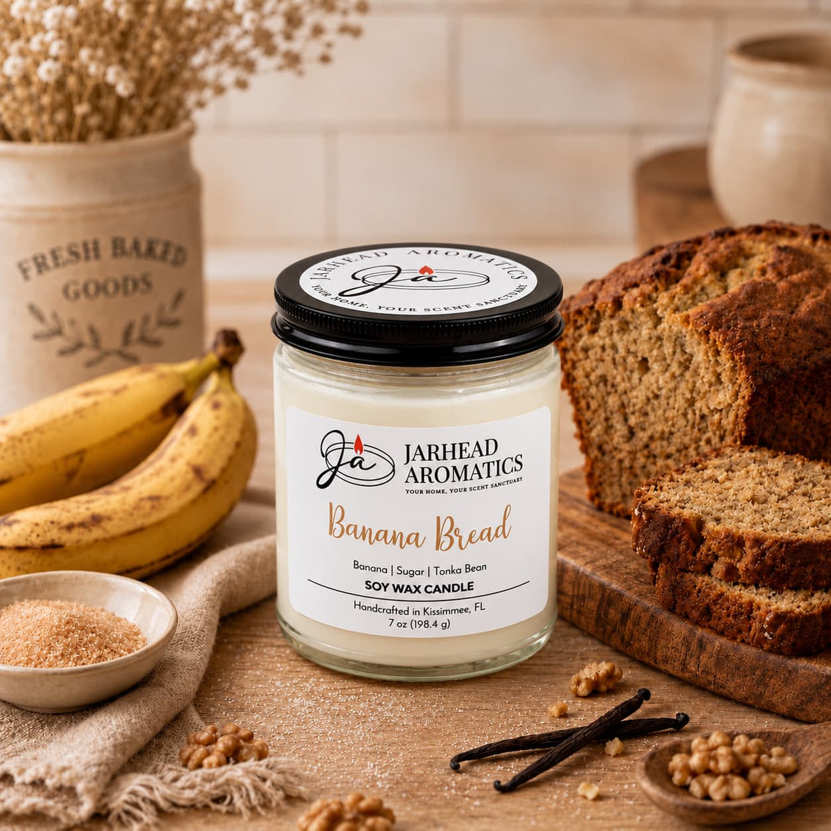 A Jarhead Aromatics Banana Bread Soy Wax Candle | Banana, Sugar & Tonka Bean sits on a wooden board next to a sliced loaf of banana bread, two bananas, a small bowl of sugar, and vanilla beans.
