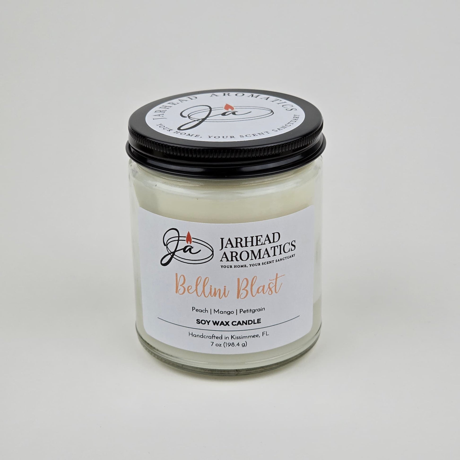 The Bellini Blast Soy Wax Candle by Jarhead Aromatics features peach, mango, and tangerine scents. This handcrafted glass jar candle has a black lid, white label, and is made in Kissimmee, FL.