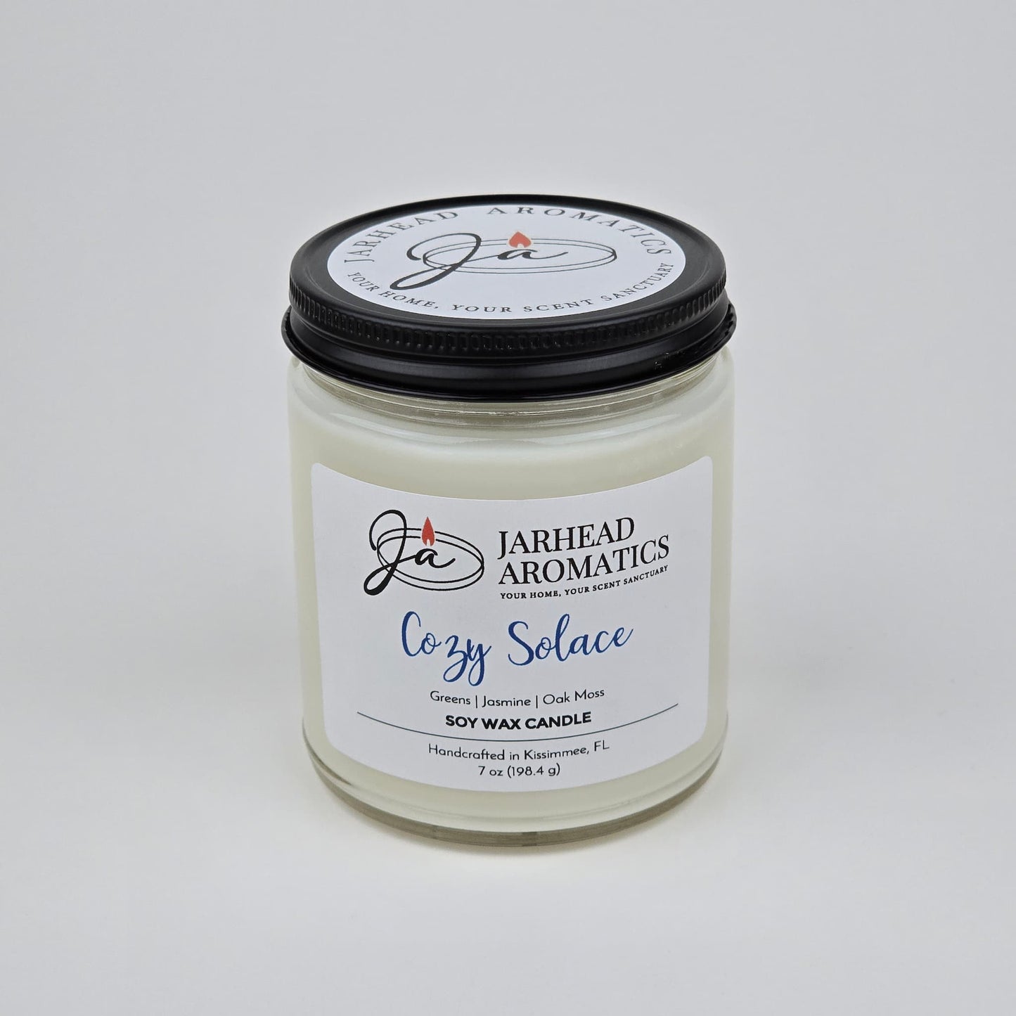 The Cozy Solace Soy Wax Candle by Jarhead Aromatics features fresh greens, jasmine, oak moss, and musk—an ideal fall scent—and comes hand-poured in a clear glass jar with a black lid.